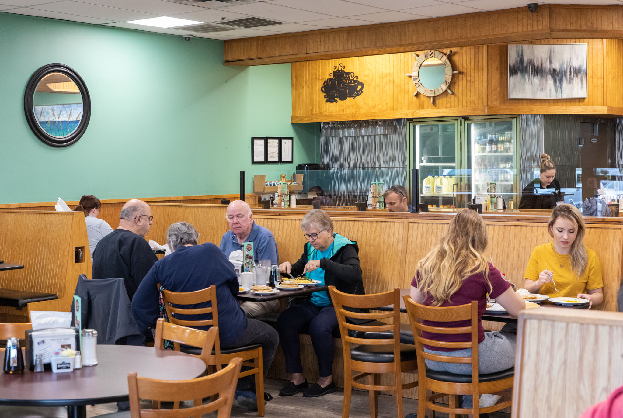 Guests enjoy their meals in a cozy, wood-accented diner with teal walls and warm lighting.