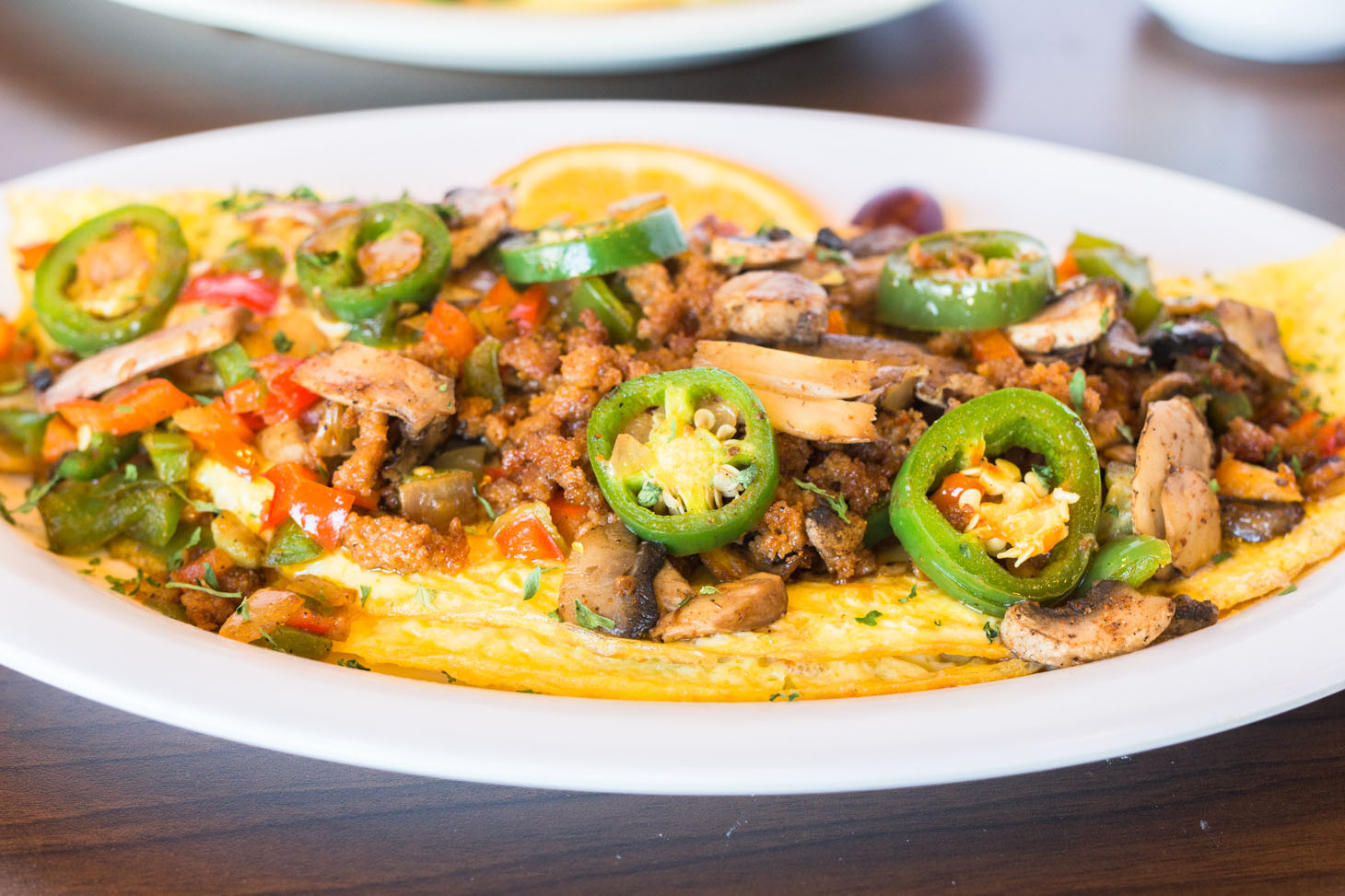 Close-up of a savory omelette topped with sautéed mushrooms, ground sausage, chopped bell peppers, and sliced jalapeños